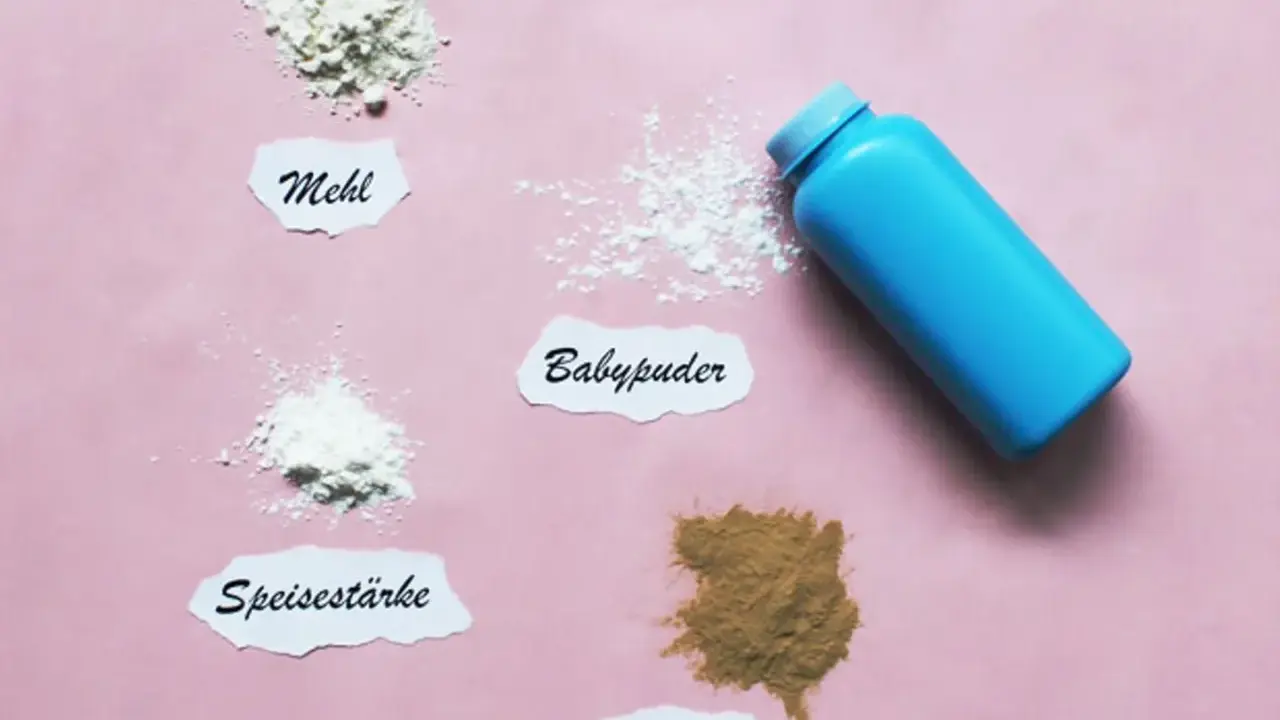 Ein blauer Behälter mit Babypuder liegt neben kleinen Häufchen von Mehl, Speisestärke und Heilerde. Babypuder als Trockenshampoo ist eine schnelle Lösung.