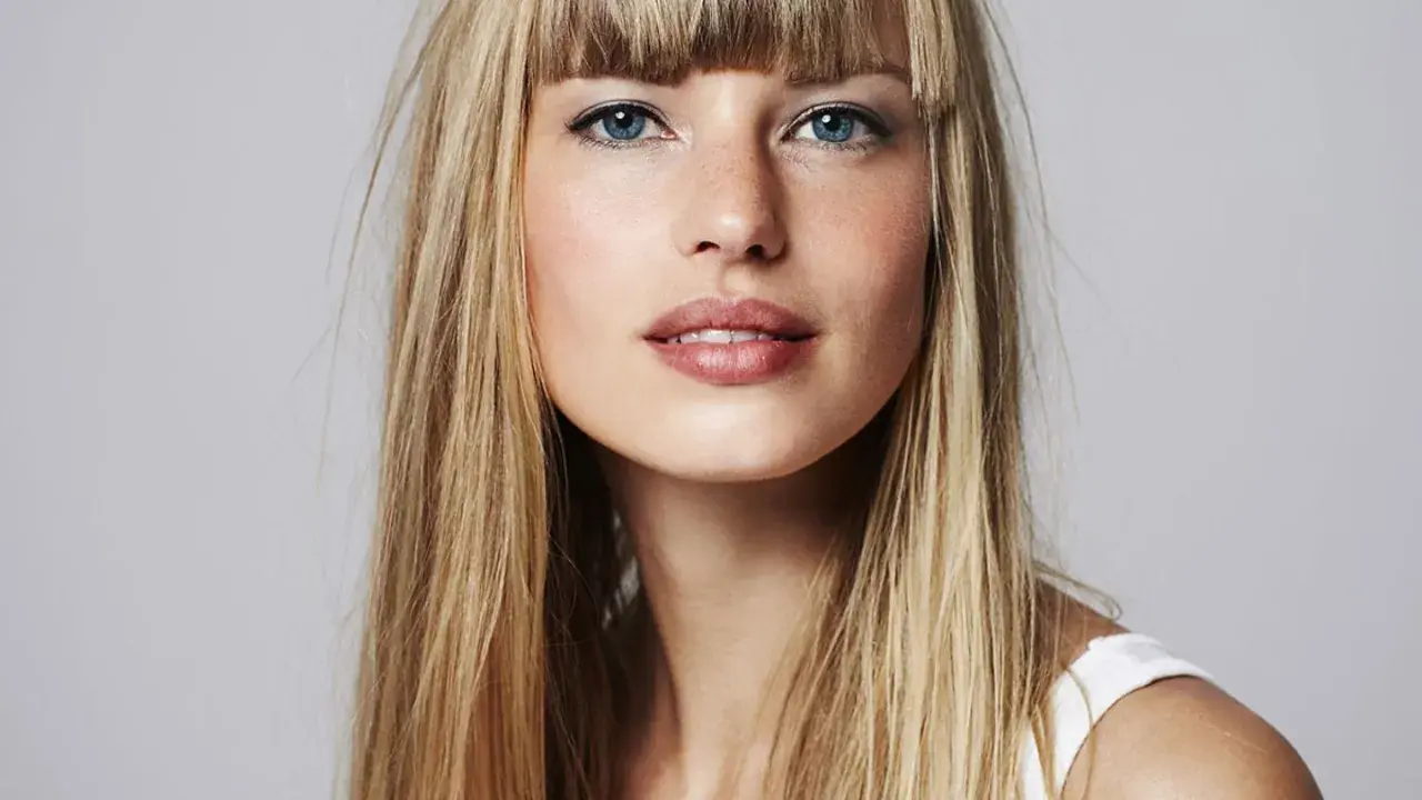 Blonde Frau mit auffälligem Buzz Cut und blauen Augen, die direkt in die Kamera blickt.