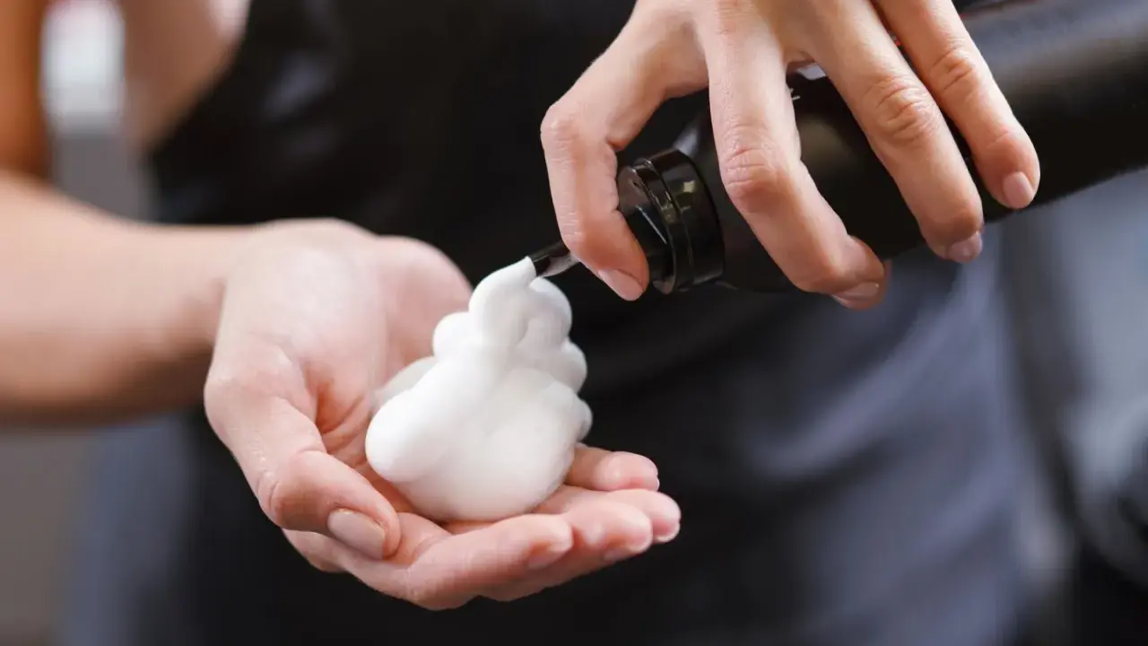 Schaumfestiger Anwendung: Eine Hand hält eine Flasche, aus der weißer Schaum in die andere Hand fließt.