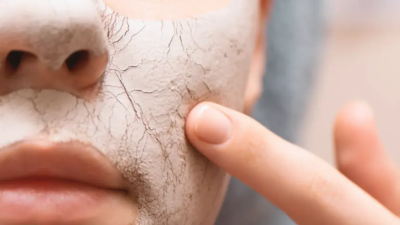 Nahaufnahme eines Gesichts mit einer trockenen, rissigen Maske. Ein Finger berührt sanft die Haut, um zu zeigen, wie man trockene Haut von innen behandeln kann.