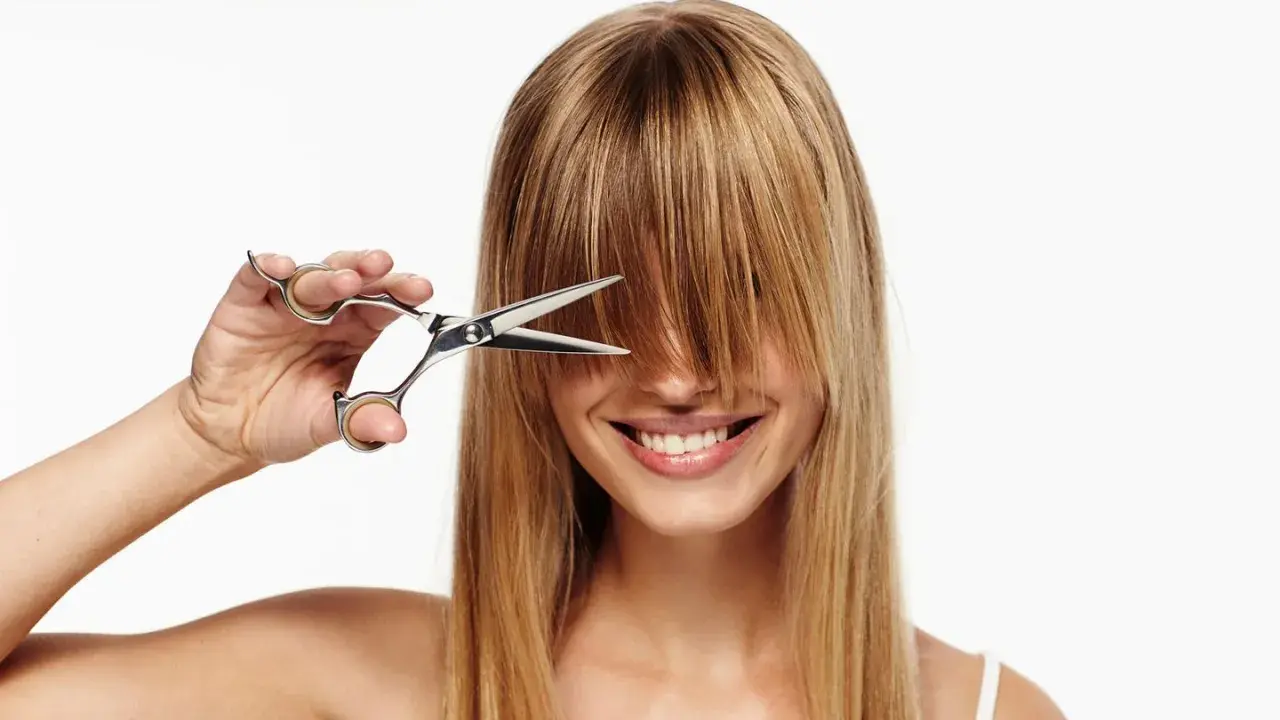 Frau mit Schere im blonden Haar, bereit, sich die Haare selber zu schneiden.