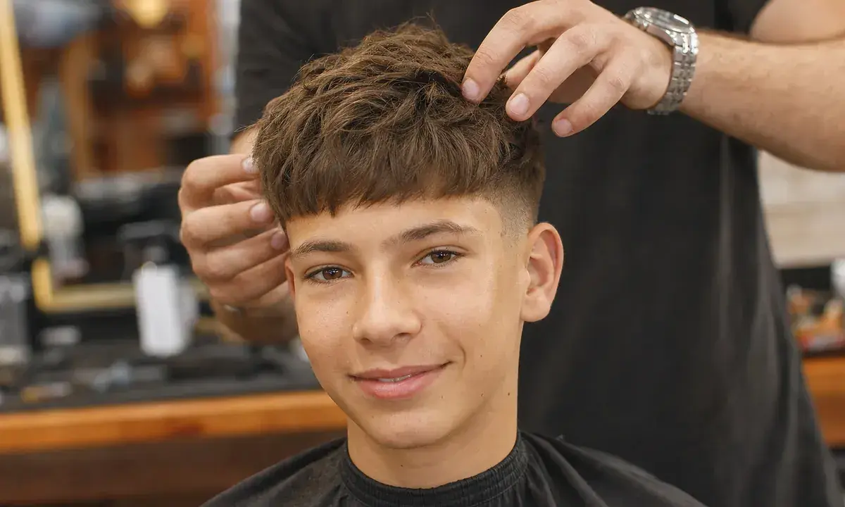 Ein Junge mit einem modernen Haarschnitt, der von einem Friseur gestylt wird. Tolle Frisuren für Jungs!