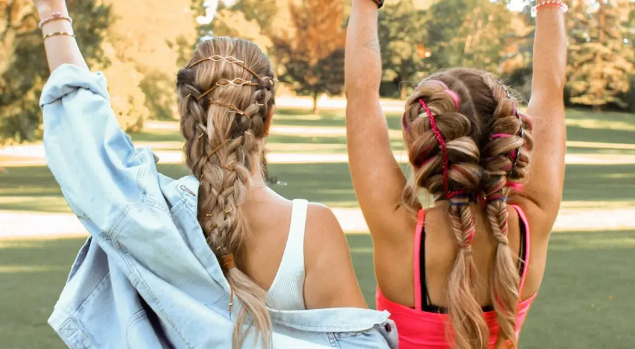 Zwei Freundinnen mit aufwendigen Festival Frisuren, Zöpfen mit Lederbändern und bunten Fäden, genießen die Sonne.