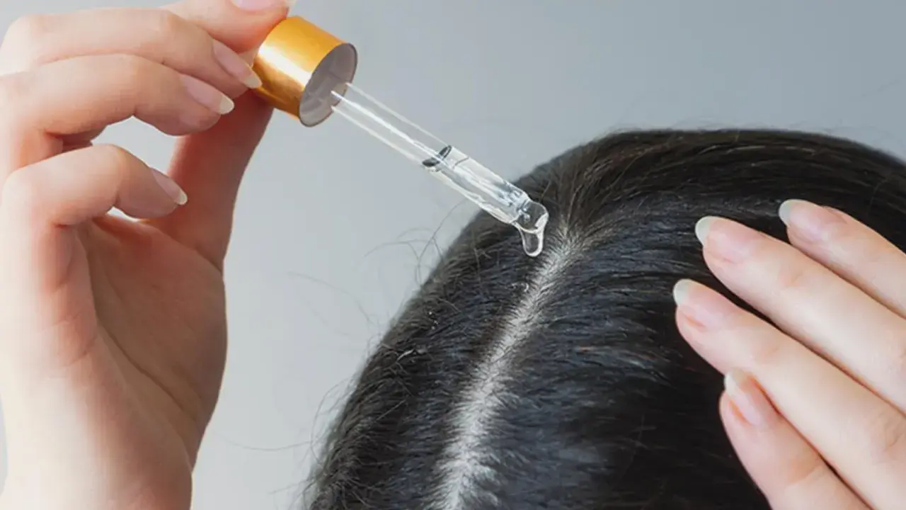 Eine Hand trägt mit einer Pipette Öl auf die Kopfhaut auf, um trockene Kopfhaut mit Hausmitteln zu behandeln.