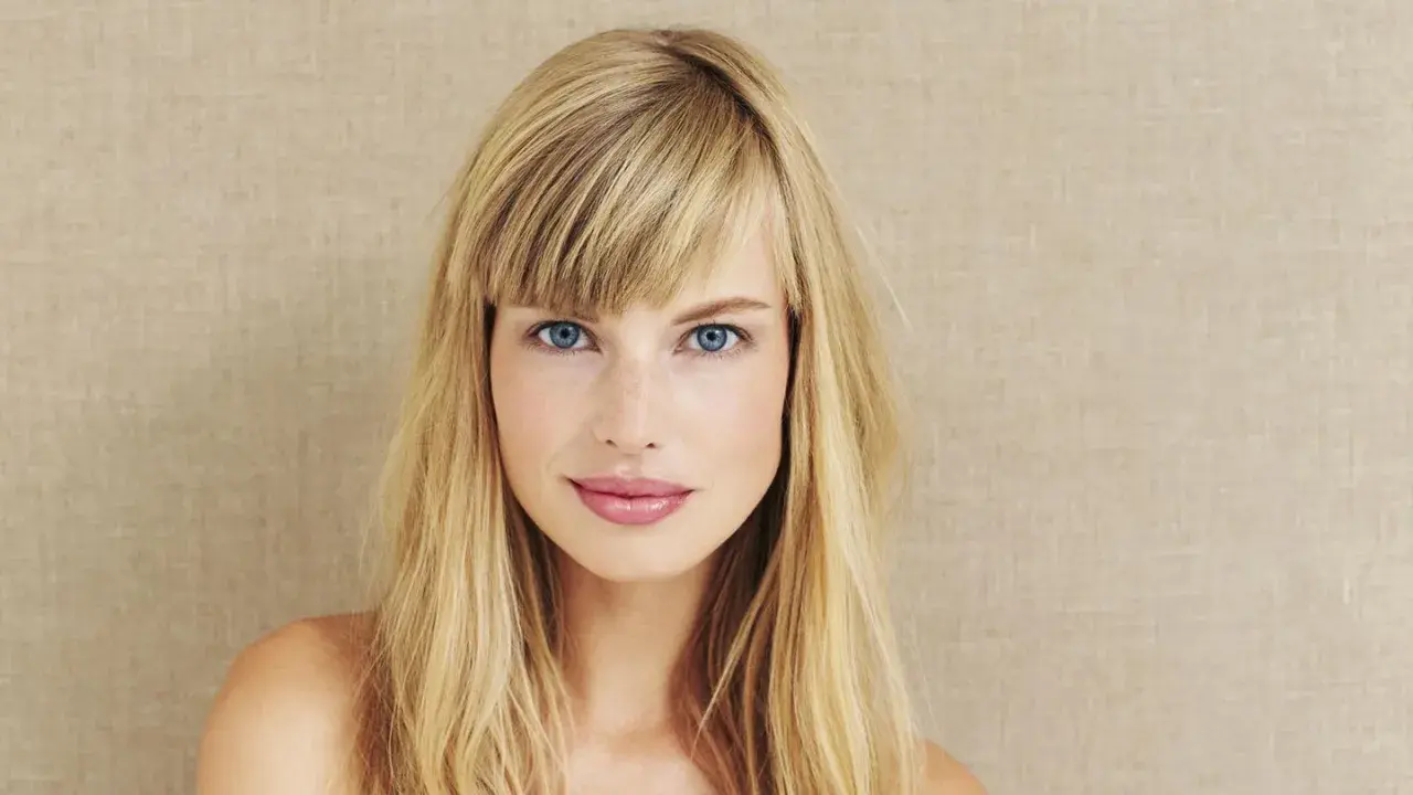 Blonde Frau mit blauen Augen und einem lässigen Pony, der aussieht, als hätte sie ihn selber geschnitten.