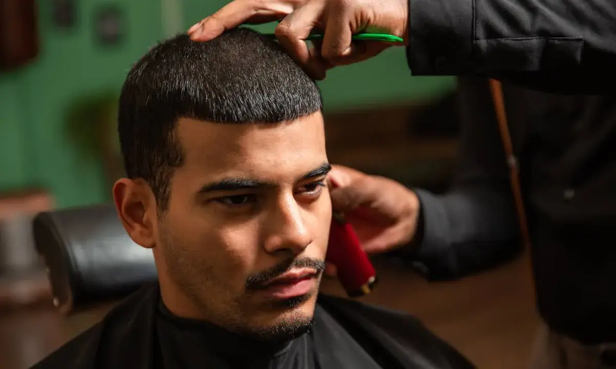 Ein Mann bekommt einen **langer buzz cut** beim Friseur. Die Haare werden mit einer Schere und einem Trimmer in Form gebracht.