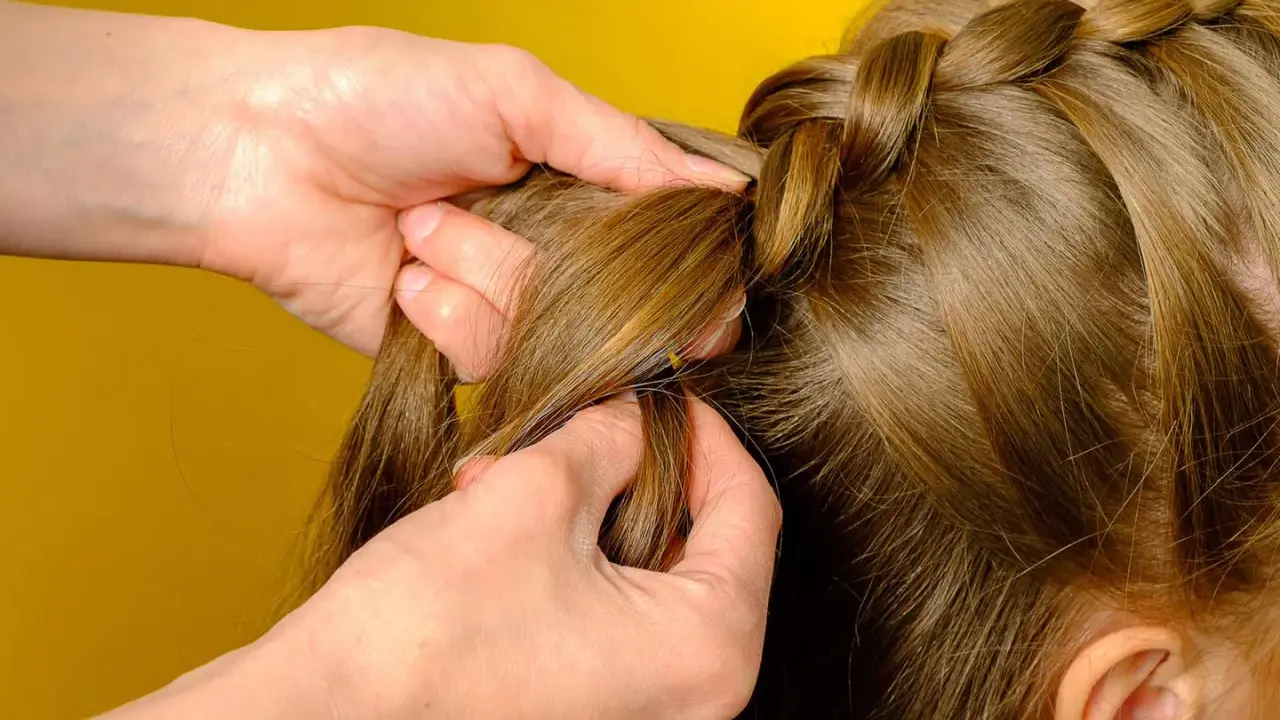 Hände flechten einen Bauernzopf. Die Haare werden sorgfältig zu einem kunstvollen Zopf geflochten, der an traditionelle Frisuren erinnert.