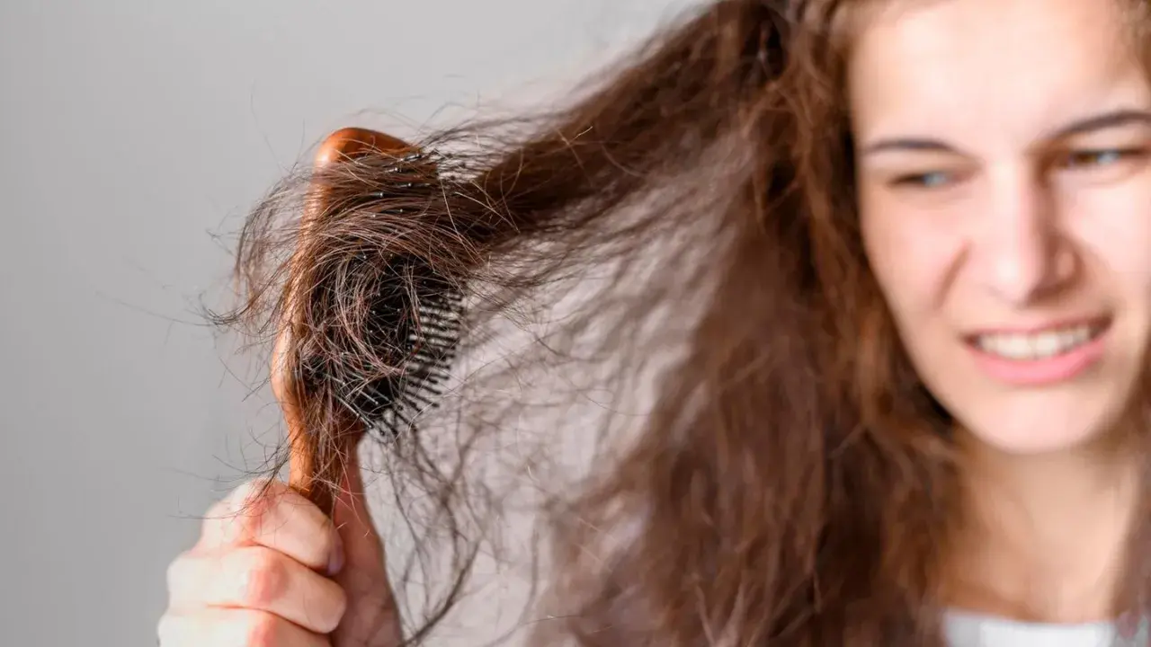 Verzweifelt versucht eine junge Frau, ihre strohigen Haare nach einer Keratinbehandlung zu kämmen. Die Bürste verheddert sich in den widerspenstigen Strähnen.