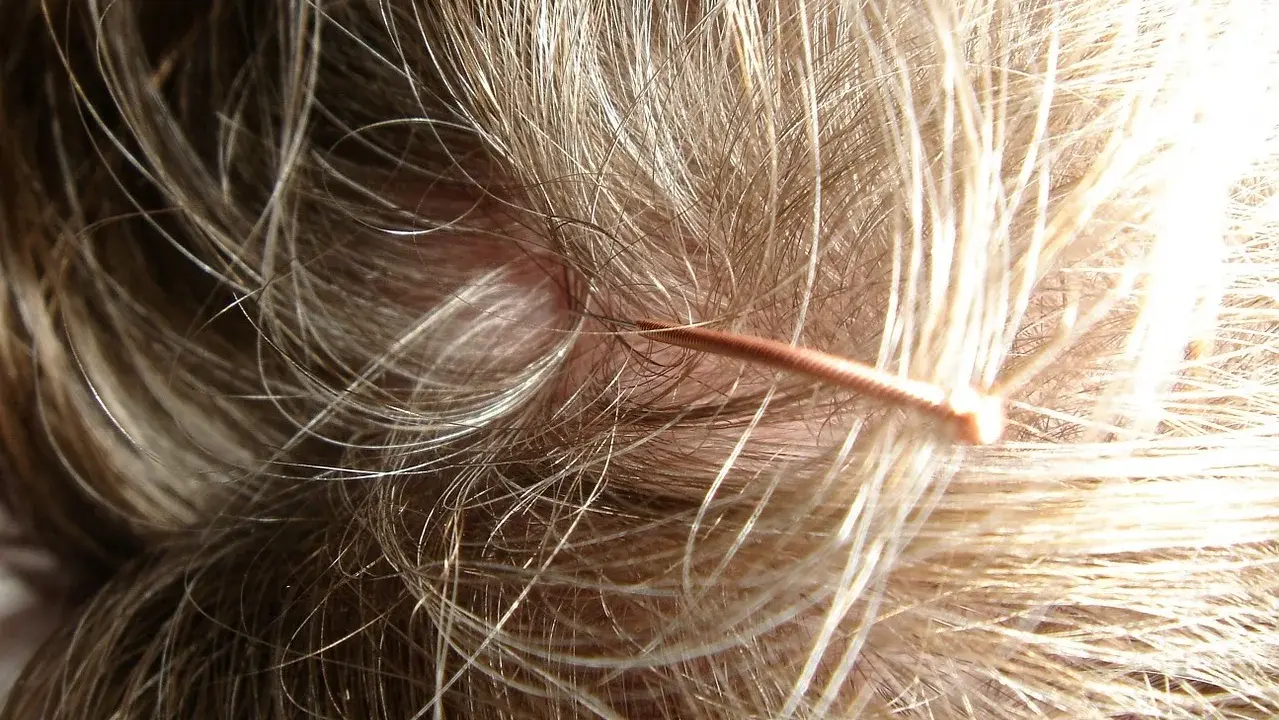 Nahaufnahme einer juckenden Kopfhaut mit feinen Haaren und einer dünnen, kupferfarbenen Haarschnecke.