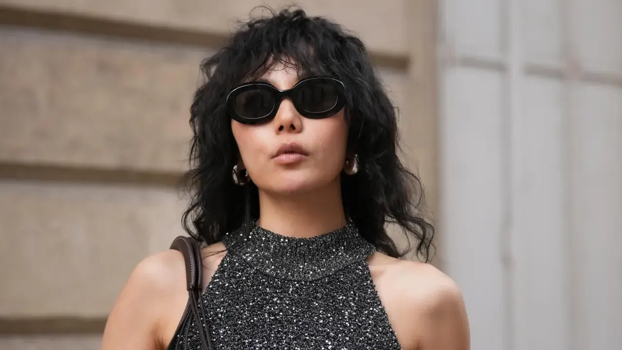 Frau mit schulterlangem Wolf Cut, Sonnenbrille und glitzerndem Top.