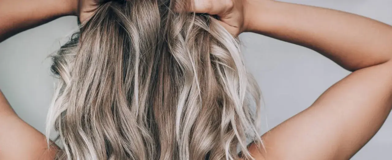 Hände im blonden, drahtigen Haar, das in Wellen fällt.
