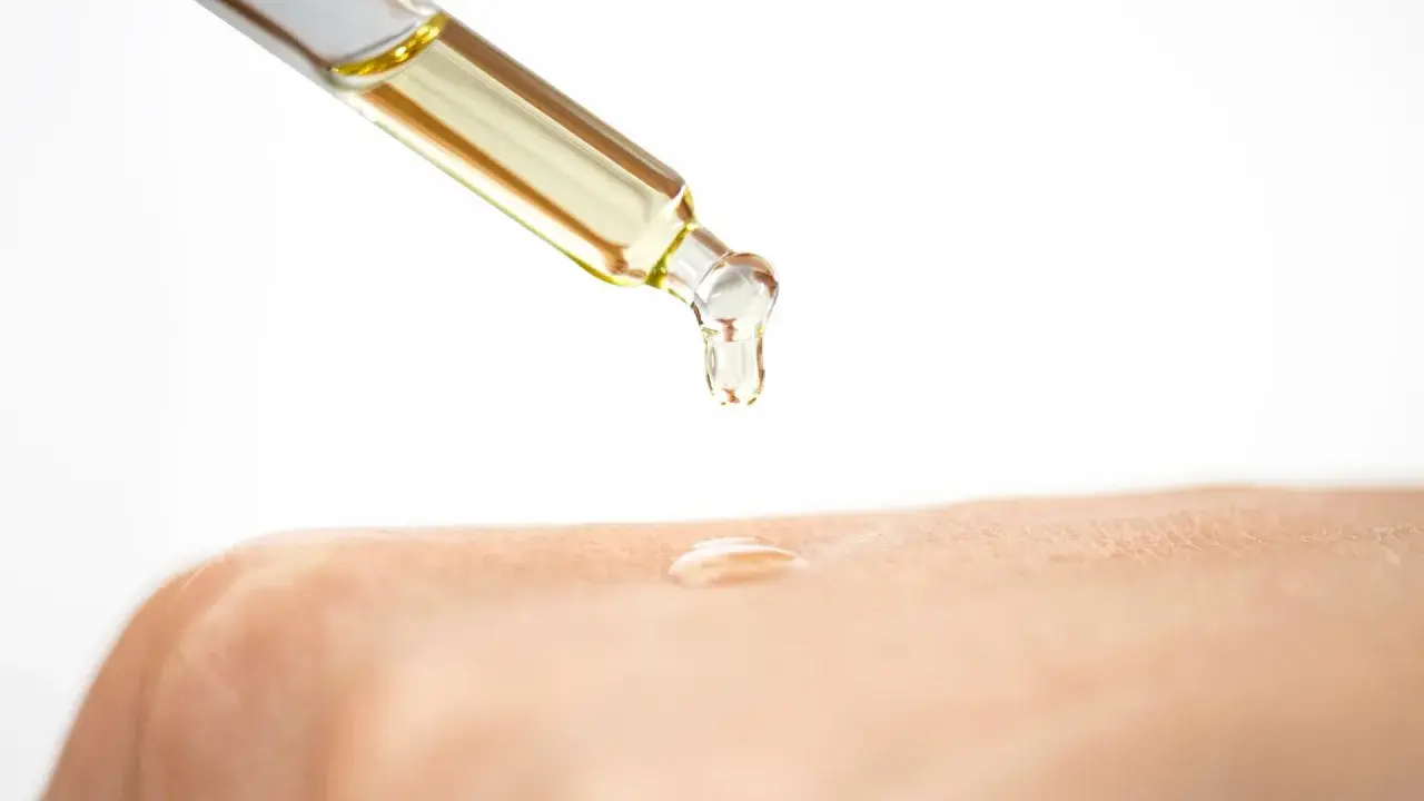 Ein Tropfen Öl fällt aus einer Pipette auf die Haut. Die Glycerin Wirkung auf die Haut wird hier gezeigt: Feuchtigkeit und Geschmeidigkeit.