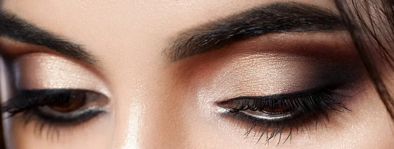 Nahaufnahme eines geschminkten Auges. Ein schimmernder Lidschatten wurde aufgetragen, mit einem dramatischen dunklen Smokey-Eye-Effekt.