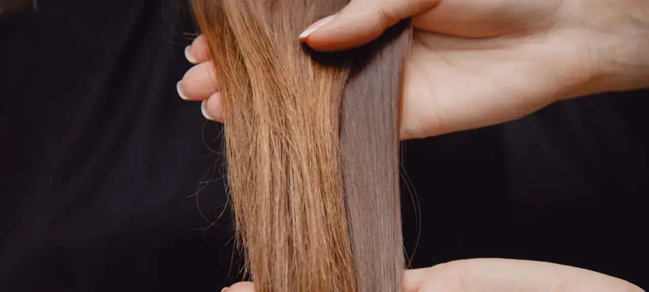 Hände halten zwei Strähnen Haar. Eine ist hellbraun und wirkt etwas struppig, die andere ist dunkler und glänzt. So bekomme ich glanz in meine haare.