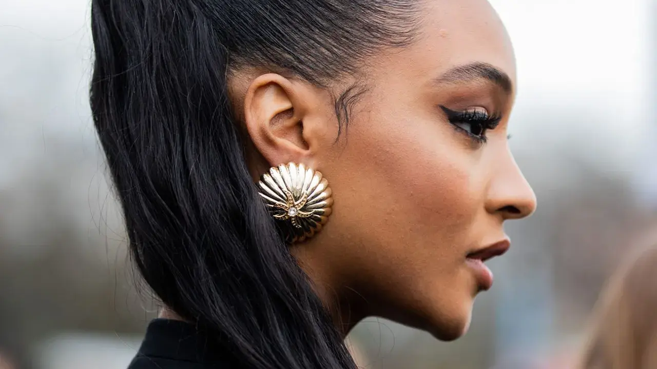 Ein scharfer Cat-Eye-Liner betont die Augen, perfekt aufgetragen mit Kajal. Goldene Muschel-Ohrringe und ein hoher Pferdeschwanz runden den Look ab.
