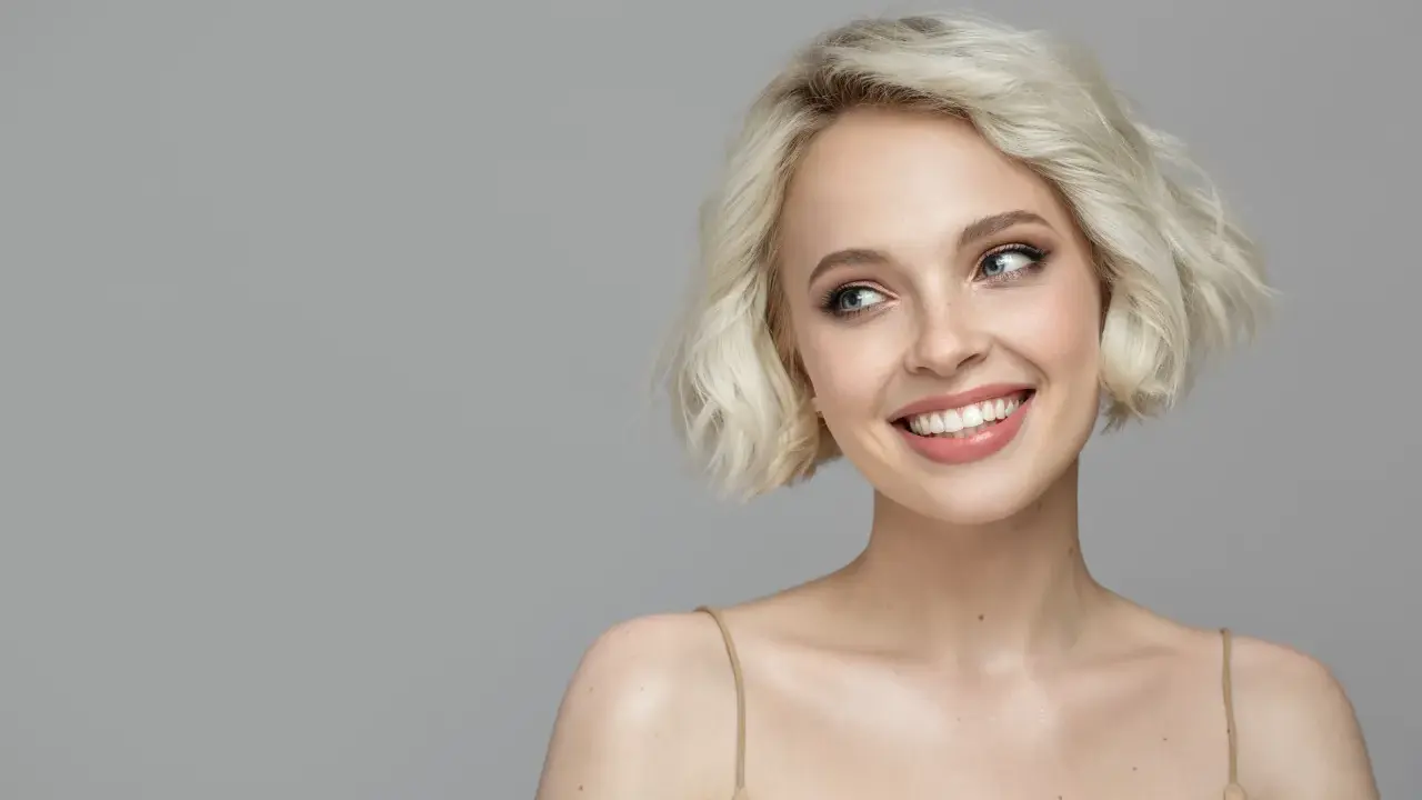 Lächelnde Frau mit sehr feinem Haar, das zu einem kurzen Bob gestylt ist. Ihre blauen Augen blicken nach links.