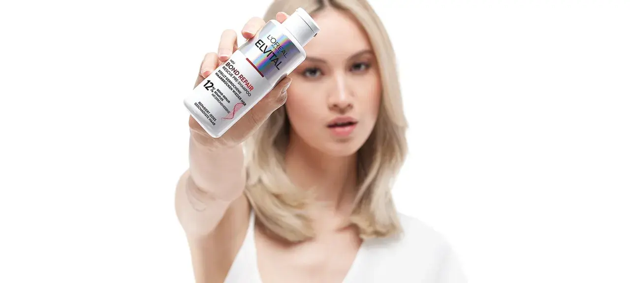 Frau hält L'Oréal Elvital Bond Repair Pre-Shampoo. Ideal für die Haarpflege bei trockenem Haar, repariert es geschädigte Haarbrücken.