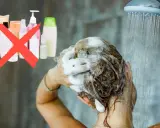 Frau wäscht sich die Haare unter der Dusche, Schaum im Haar. Eine rote durchgestrichene Gruppe von Shampoo-Flaschen deutet auf haare waschen ohne shampoo hin.