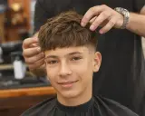 Ein Junge mit einem modernen Haarschnitt, der von einem Friseur gestylt wird. Tolle Frisuren für Jungs!