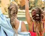 Zwei Freundinnen mit aufwendigen Festival Frisuren, Zöpfen mit Lederbändern und bunten Fäden, genießen die Sonne.