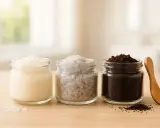 Drei Gläser mit Zutaten für ein Peeling selber machen trockene Haut: eine cremige Masse, Salzkristalle und Kaffeesatz.