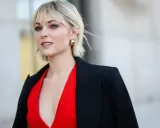 Blonde Frau mit einem frechen Bixie Cut, rotem Kleid und schwarzem Blazer.