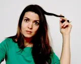 Frau mit überraschtem Gesichtsausdruck, die eine Strähne ihrer aufgeladenen Haare verdreht.
