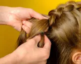 Hände flechten einen Bauernzopf. Die Haare werden sorgfältig zu einem kunstvollen Zopf geflochten, der an traditionelle Frisuren erinnert.