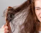 Verzweifelt versucht eine junge Frau, ihre strohigen Haare nach einer Keratinbehandlung zu kämmen. Die Bürste verheddert sich in den widerspenstigen Strähnen.