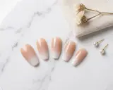 Fünf elegante Ombre-Nägel mit sanftem Farbverlauf von Nude zu Weiß, daneben Perlenohrstecker und getrocknete Blumen.