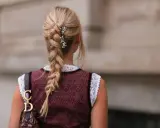 Blonde Zopf-Frisur mit Blumen-Akzenten, perfekt für Oktoberfest-Frisuren. Ein Dirndl und eine Dior-Tasche runden den Look ab.