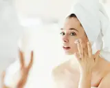Frau mit Handtuch auf dem Kopf trägt Creme auf, um trockene Haut im Winter zu pflegen.