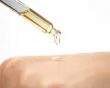 Ein Tropfen Öl fällt aus einer Pipette auf die Haut. Die Glycerin Wirkung auf die Haut wird hier gezeigt: Feuchtigkeit und Geschmeidigkeit.
