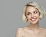 Lächelnde Frau mit sehr feinem Haar, das zu einem kurzen Bob gestylt ist. Ihre blauen Augen blicken nach links.