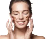 Frau mit geschlossenen Augen und einem Lächeln, die sich mit einem selbstgemachten Gesichtspeeling die Wangen massiert.