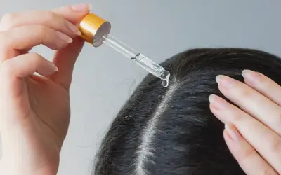 Eine Hand trägt mit einer Pipette Öl auf die Kopfhaut auf, um trockene Kopfhaut mit Hausmitteln zu behandeln.