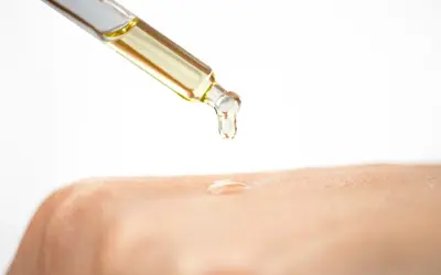 Ein Tropfen Öl fällt aus einer Pipette auf die Haut. Die Glycerin Wirkung auf die Haut wird hier gezeigt: Feuchtigkeit und Geschmeidigkeit.