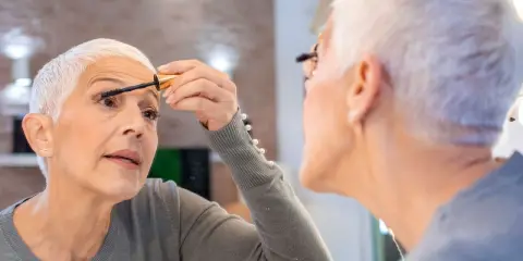 Frau über 60 schminkt sich die Wimpern, um Schlupflider zu kaschieren. Ein Tipp für ein strahlendes Augen-Make-up.