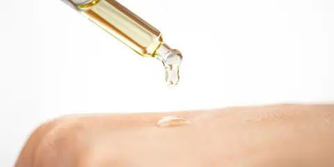 Ein Tropfen Öl fällt aus einer Pipette auf die Haut. Die Glycerin Wirkung auf die Haut wird hier gezeigt: Feuchtigkeit und Geschmeidigkeit.