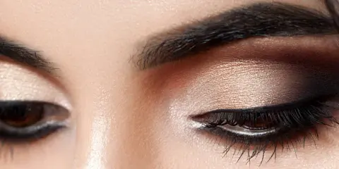 Nahaufnahme eines geschminkten Auges. Ein schimmernder Lidschatten wurde aufgetragen, mit einem dramatischen dunklen Smokey-Eye-Effekt.