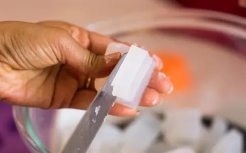 Hand schneidet klare Glycerinseife. Die Seife ist rein und wird bald auf der Haut angewendet.