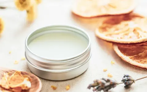 Ein Döschen mit selbstgemachtem Lippenbalsam, umgeben von getrockneten Orangen, Lavendel und Kräutern.