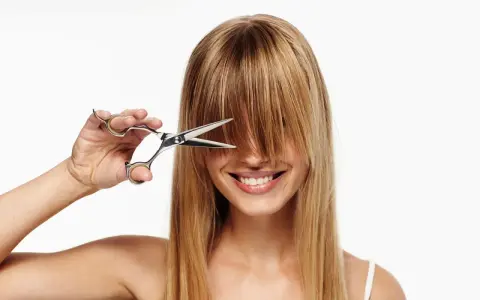 Frau mit Schere im blonden Haar, bereit, sich die Haare selber zu schneiden.