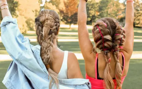 Zwei Freundinnen mit aufwendigen Festival Frisuren, Zöpfen mit Lederbändern und bunten Fäden, genießen die Sonne.