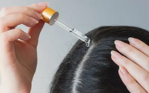 Eine Hand trägt mit einer Pipette Öl auf die Kopfhaut auf, um trockene Kopfhaut mit Hausmitteln zu behandeln.