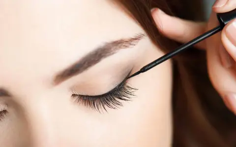 Eine Hand zieht mit schwarzem Eyeliner einen Wing für verführerische Cat Eyes.