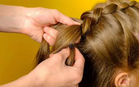 Hände flechten einen Bauernzopf. Die Haare werden sorgfältig zu einem kunstvollen Zopf geflochten, der an traditionelle Frisuren erinnert.