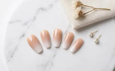 Fünf elegante Ombre-Nägel mit sanftem Farbverlauf von Nude zu Weiß, daneben Perlenohrstecker und getrocknete Blumen.