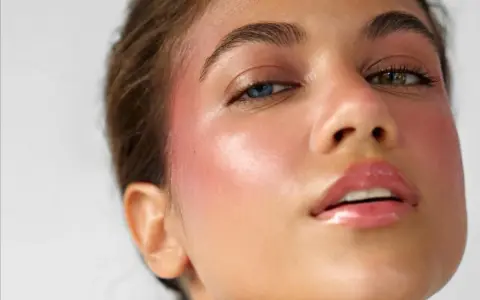 Ein **Hochzeitsgast** mit auffälligem Make-up: strahlende Haut, rosiger Blush und glänzende Lippen. Ihre Augen haben unterschiedliche Farben.