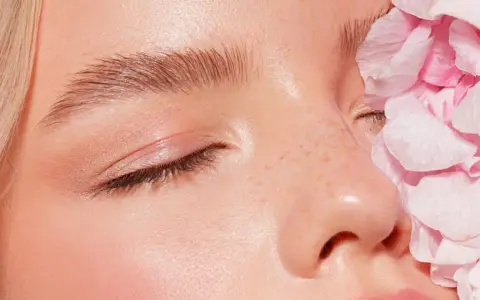 Sanftes Tages Make-up mit rosafarbenen Blütenblättern, die das Gesicht einer Frau zieren.